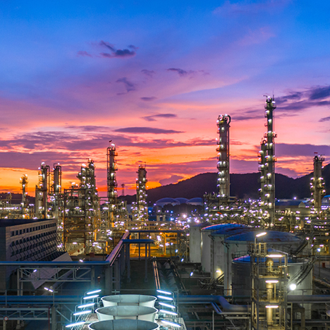 An oil refinery at sunset with mountains on the horizon.