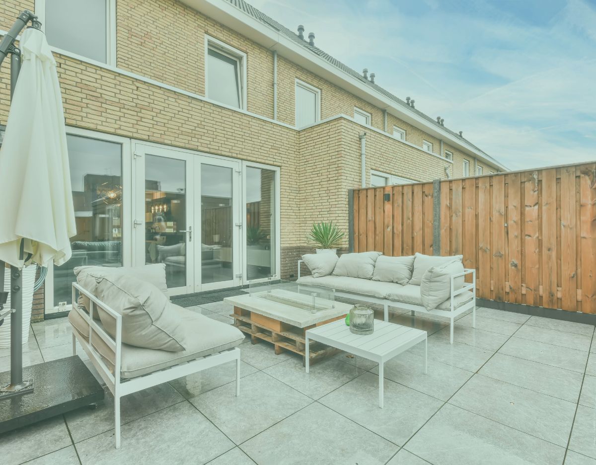 Modern outdoor patio with cushioned seating, a low coffee table, and an umbrella, set against a brick townhouse with glass doors and a wooden privacy fence.