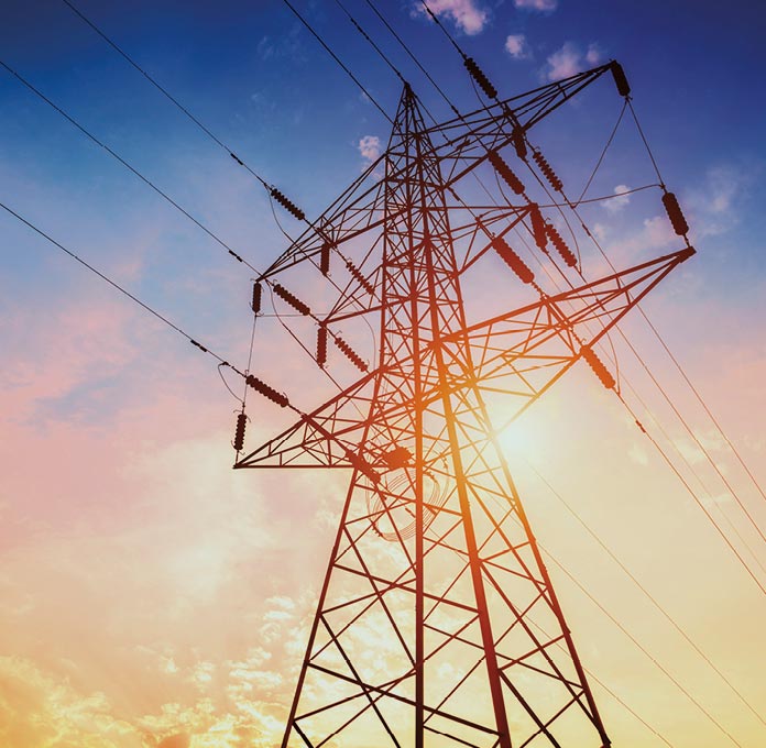 A tall electrical transmission tower with power lines, photographed against a colorful sunset sky.