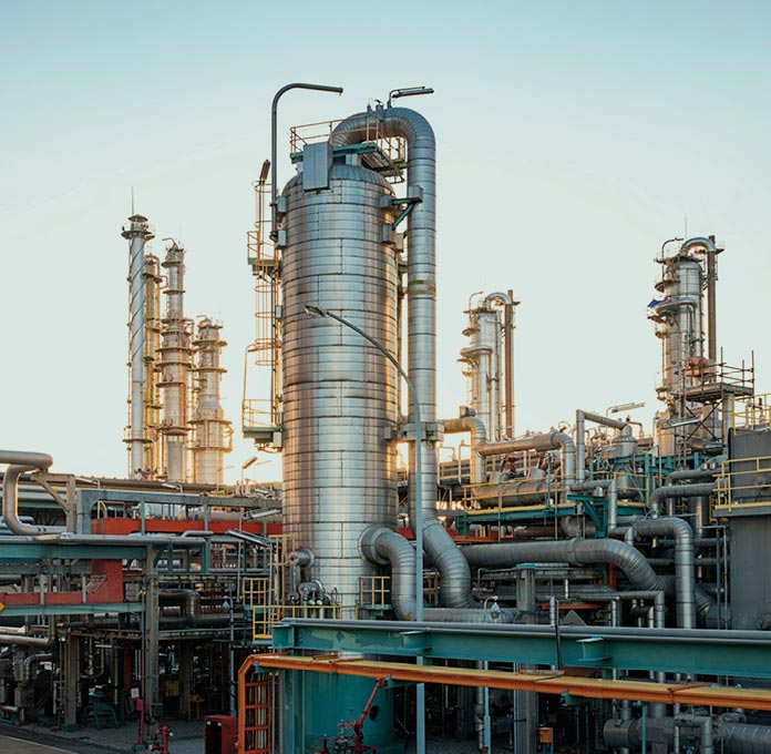Industrial refinery with multiple tall cylindrical towers, pipes, and metal structures, set against a clear sky.