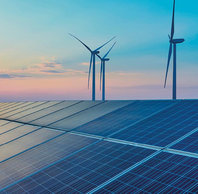 Rows of solar panels in the foreground with three wind turbines in the background under a colorful evening sky.